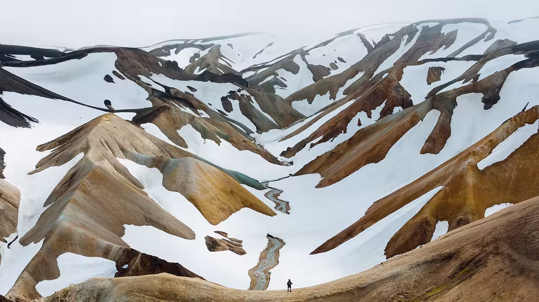 A lone hiker standing before huge snowy mountains