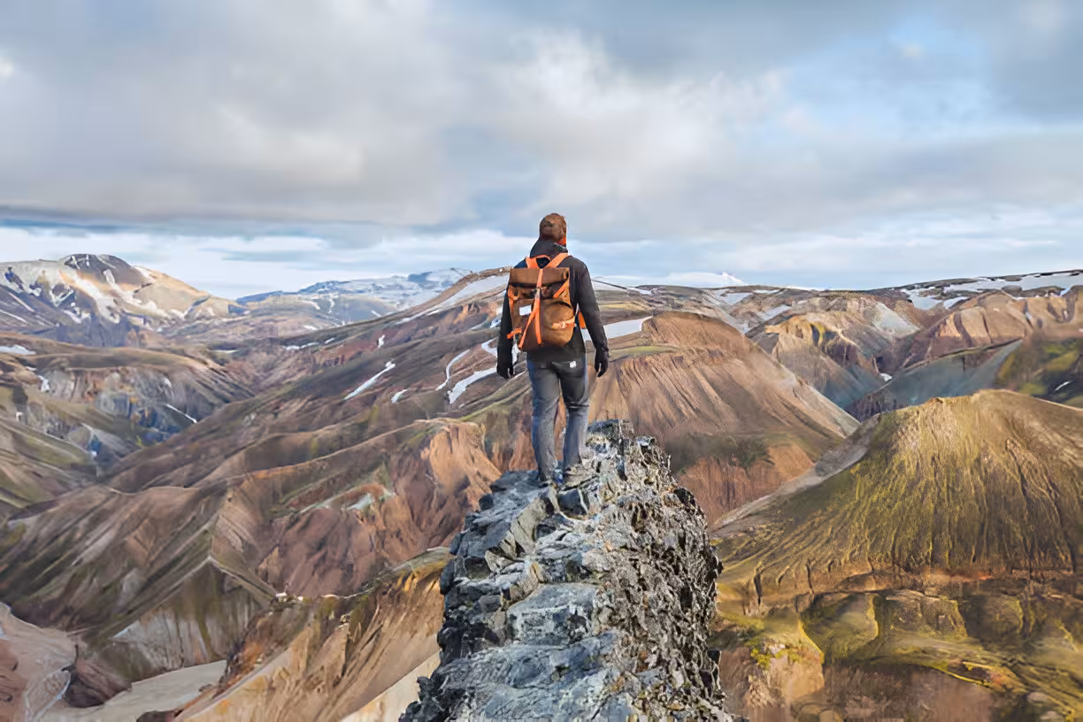 Hiker with backpack standing on rocky summit overlooking colorful Landmannalaugar mountain landscape Iceland