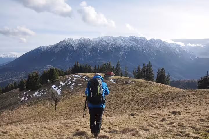 Hiker with backpack and trekking pole walking toward snow-capped Taga Mountains near Brasov
