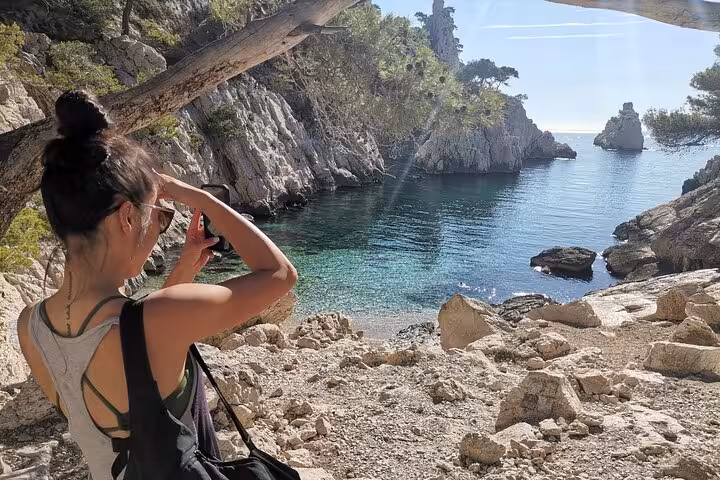 Hiker photographing turquoise Calanques cove on guided hike from Marseille in Calanques National Park