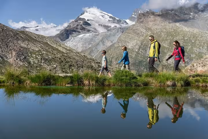 Hikers by alpine lake with Allalin glacier views near Saas-Fee, Zurich day trip to the highest revolving restaurant