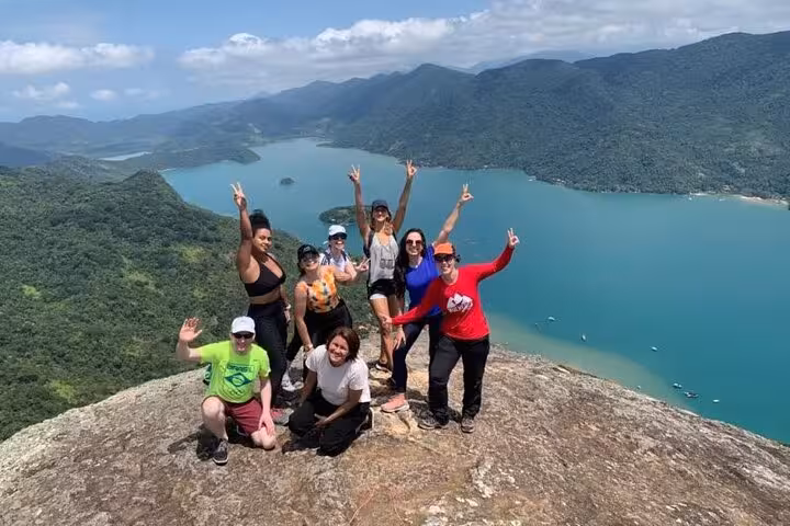 Group of hikers celebrate atop Peak Sugar Bread, capturing unforgettable views of vibrant forested mountains and clear waters.