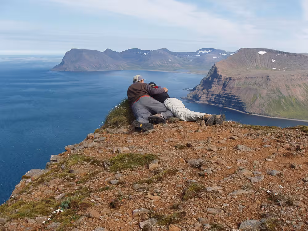Hikers resting on a dramatic cliff overlooking blue fjords on the Lost Fjords tour, remote Westfjords, Iceland