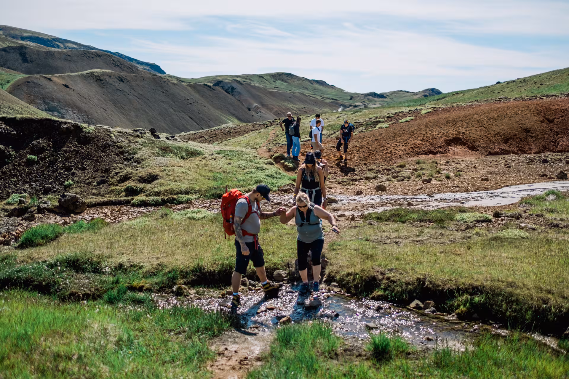 Hikers crossing a shallow stream in Iceland's geothermal valley near Hengill Volcano on a guided tour
