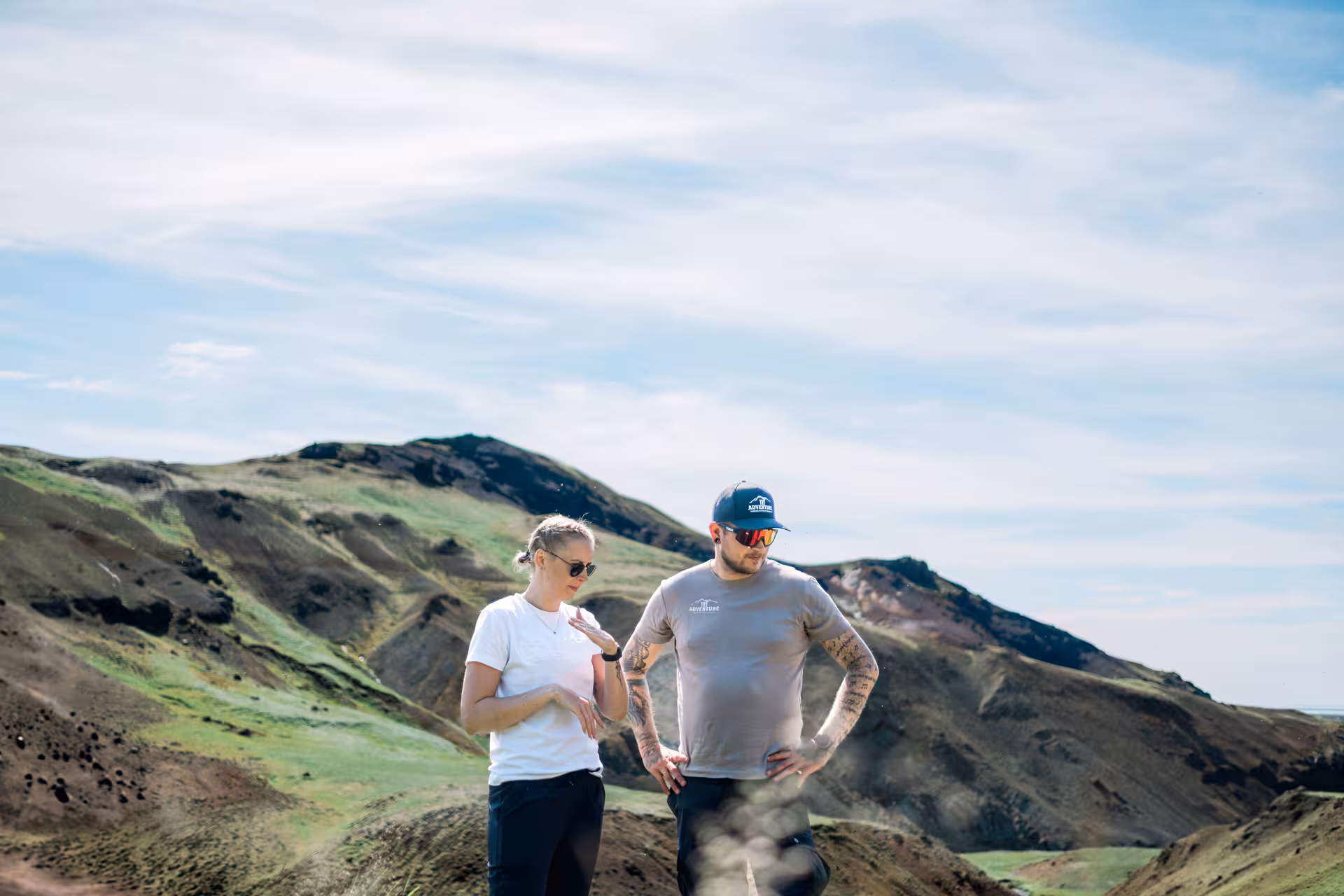 Two hikers in casual gear discussing route on volcanic ridge near Hengill geothermal valley, Iceland