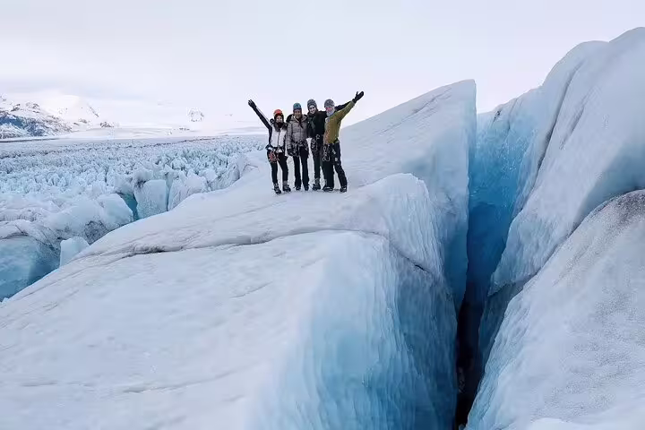 Excited group of hikers standing atop a massive glacier crevasse during Glacier Lagoon adventure tour