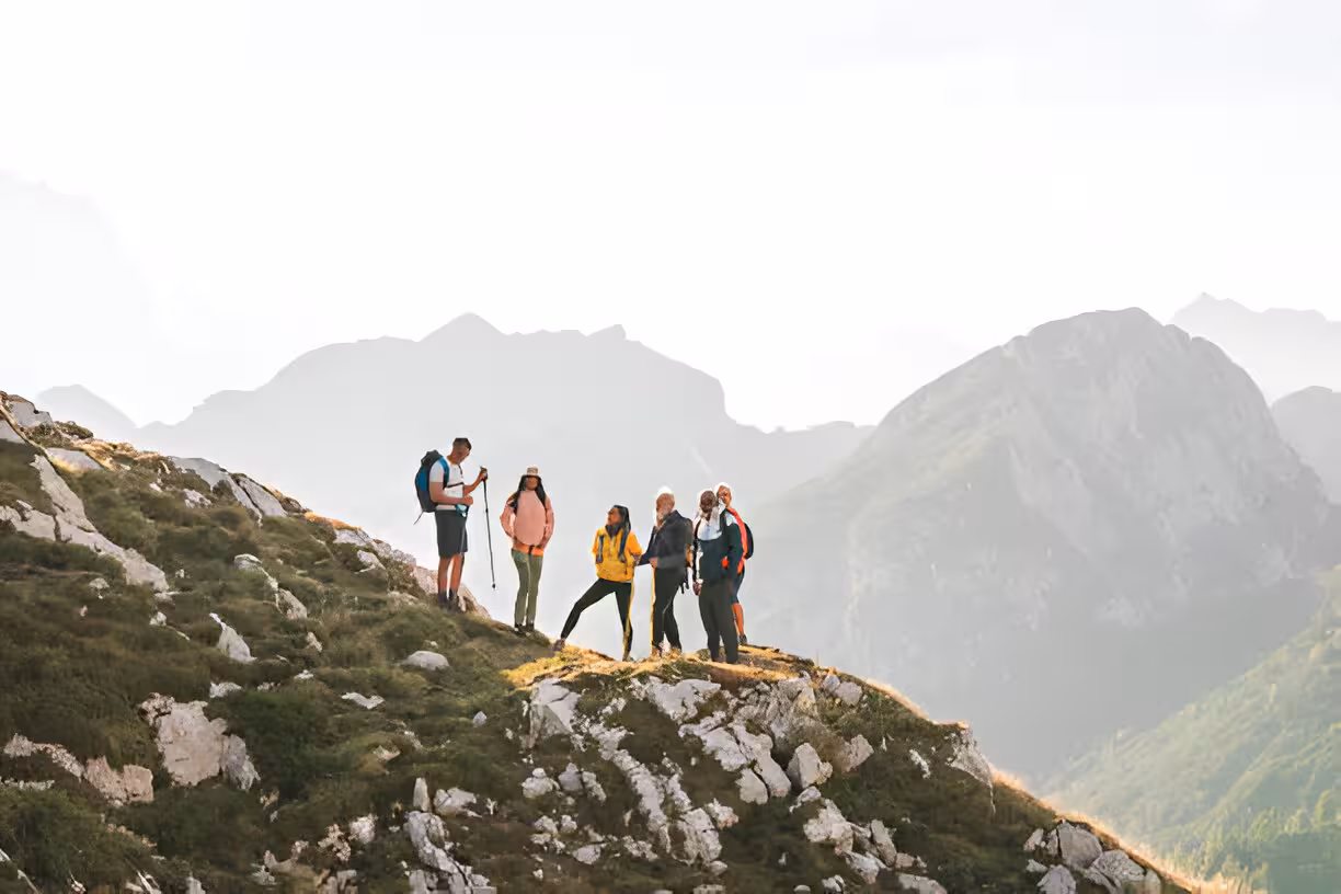 Group of hikers standing on a rocky mountain ridge with misty peaks in the background