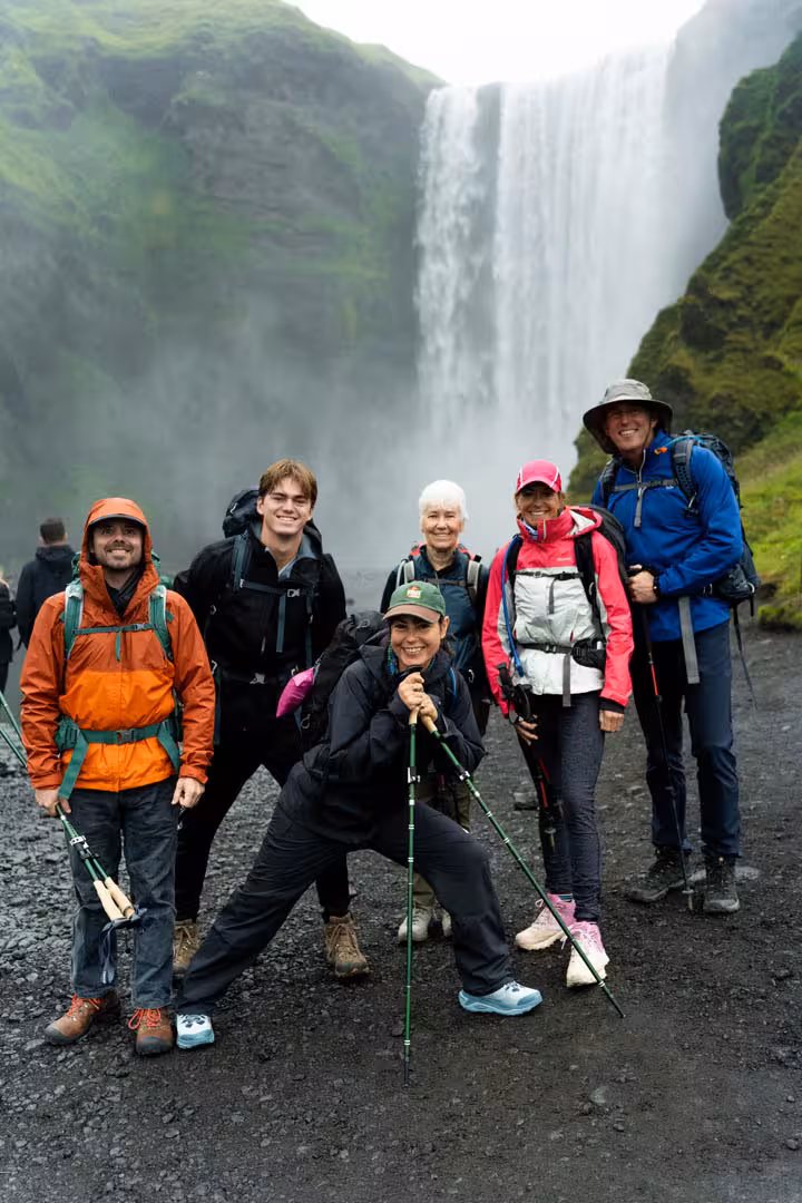 Group of six hikers with trekking poles posing in front of Skógafoss waterfall in Iceland