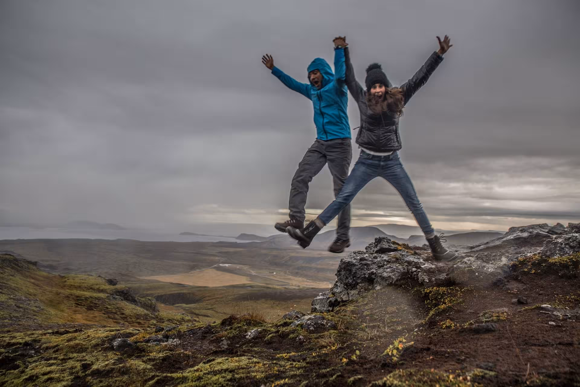 Two hikers jumping with arms raised on rocky highland terrain during Diamond Circle day trip from Akureyri