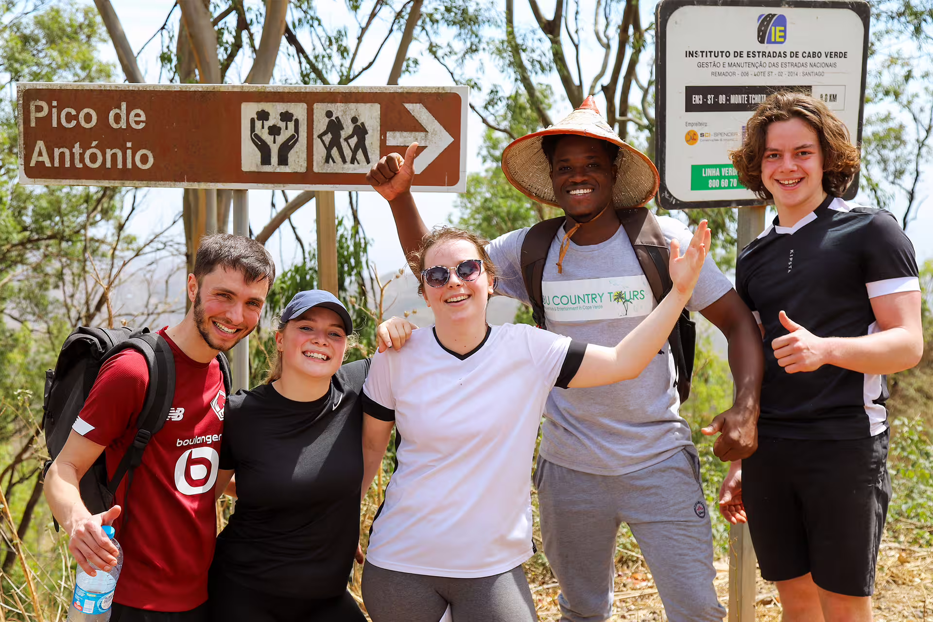 Group of hikers smiling by Pico D'Antónia sign in Monte Tchota Natural Park, Santiago's highest summit tour.