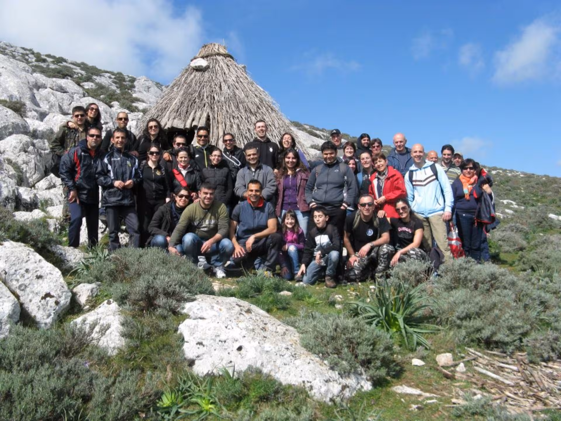 Group of hikers posing in front of traditional hut on Punta Cupeti trail, Montalbo, under a clear blue sky.