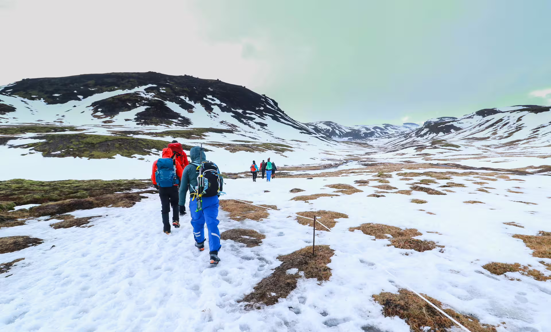 Hikers trek through snowy Reykjadalur Valley, Iceland, towards the steaming hot river, surrounded by breathtaking winter landscapes.