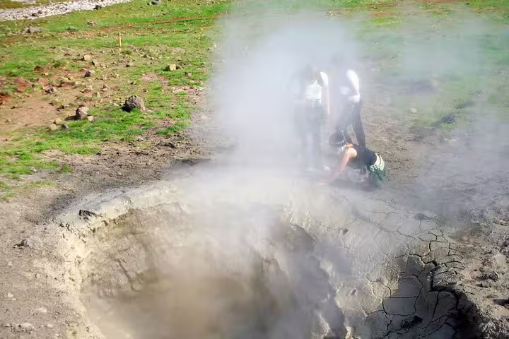 Hikers explore a steaming geothermal hot spring in Reykjadalur Valley, Iceland, surrounded by lush green landscape.