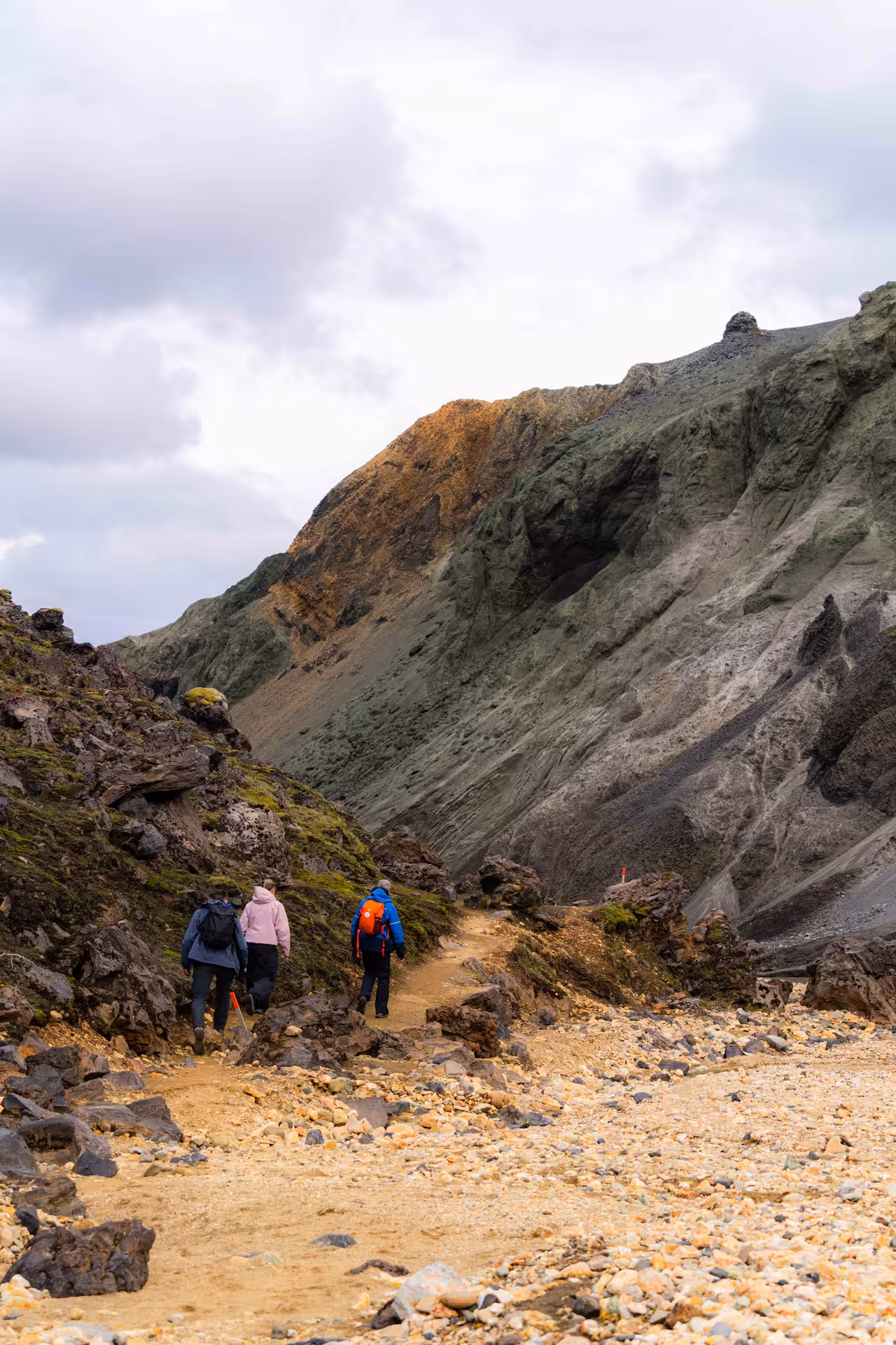 Three hikers walking a rocky trail toward colorful rhyolite mountains at Landmannalaugar Highlands
