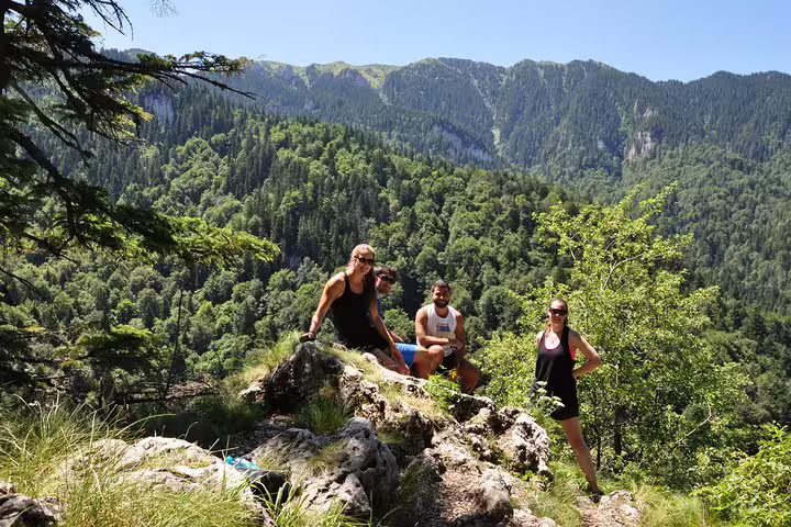 Three hikers posing on rocky outcrop with dense forested mountain canyon in background near Brasov