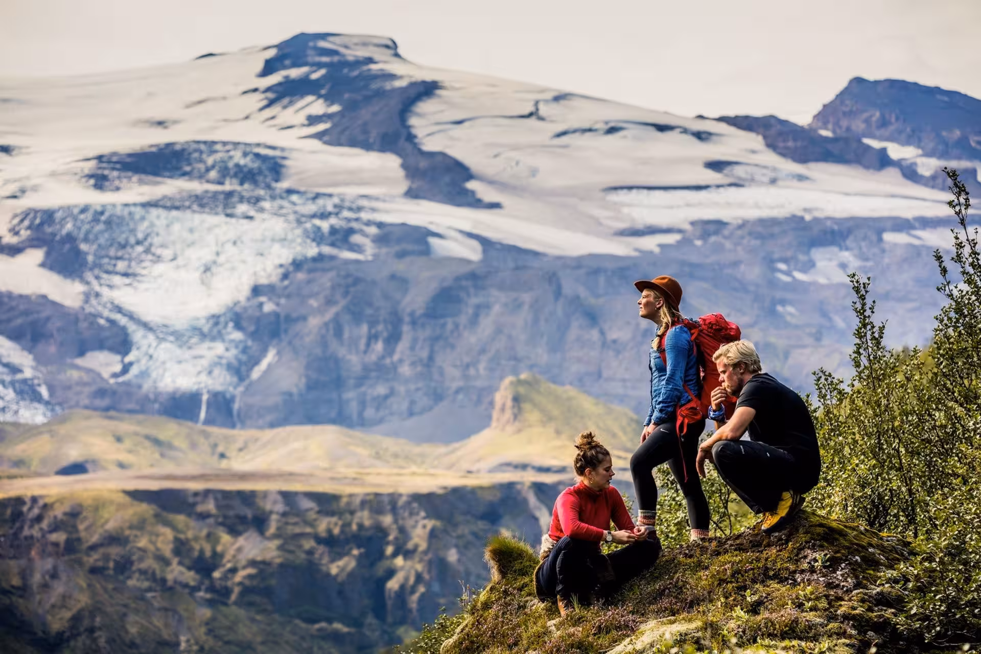 Three hikers resting on a rocky outcrop with Thorsmork glacier and green valleys in the background