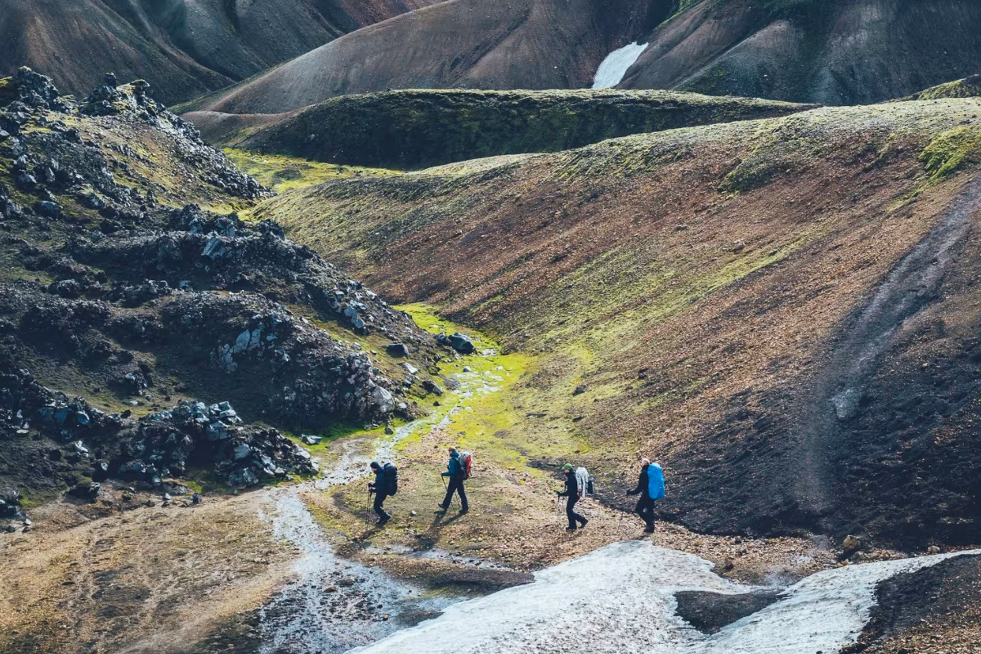 Four hikers with backpacks trekking through Landmannalaugar Iceland Highlands volcanic landscape