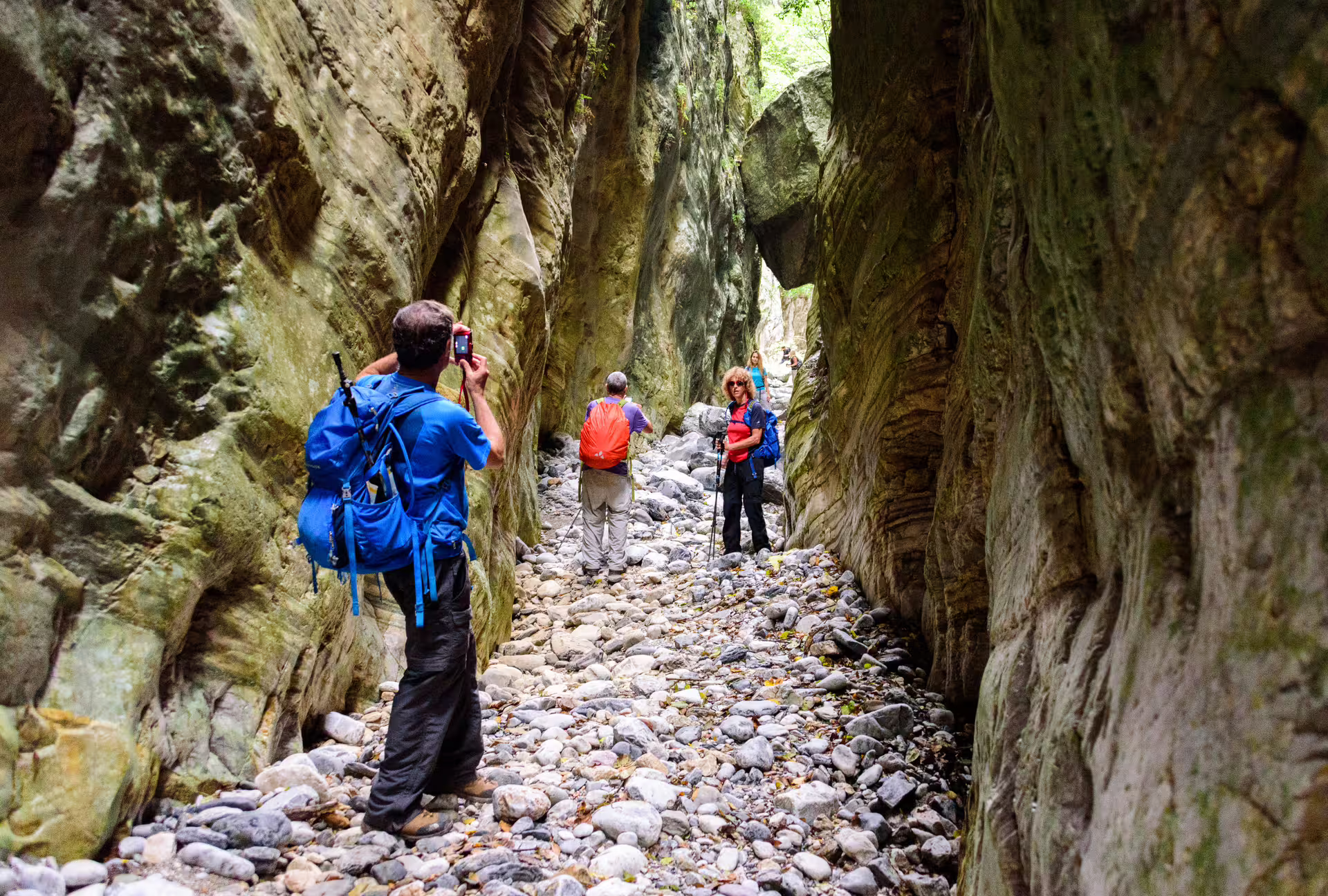 Hikers trekking through Ridomo Gorge on a guided canyon hike, walking a rocky riverbed between towering cliffs