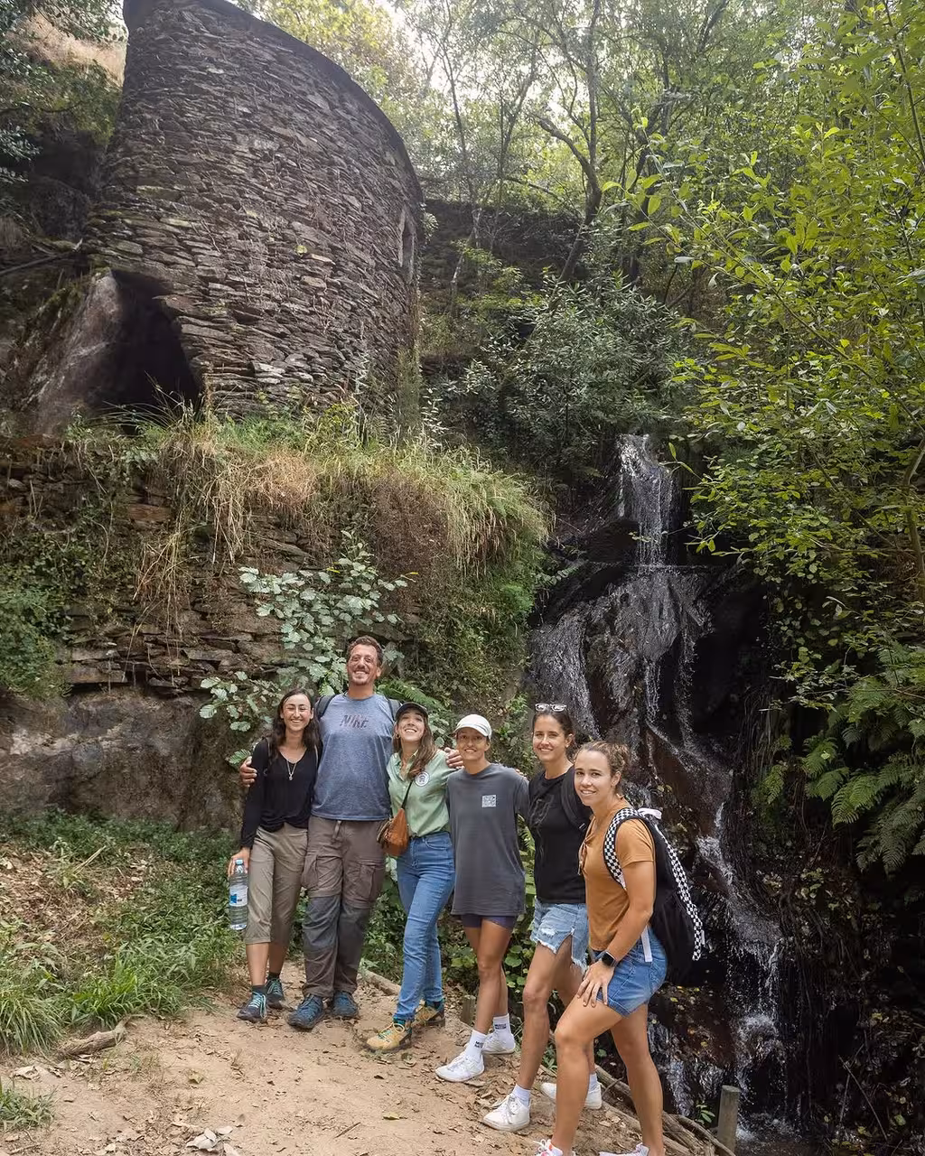 Hikers pose by a forest waterfall on the Jeeptour nature hike and yoga class with vintage car transfer