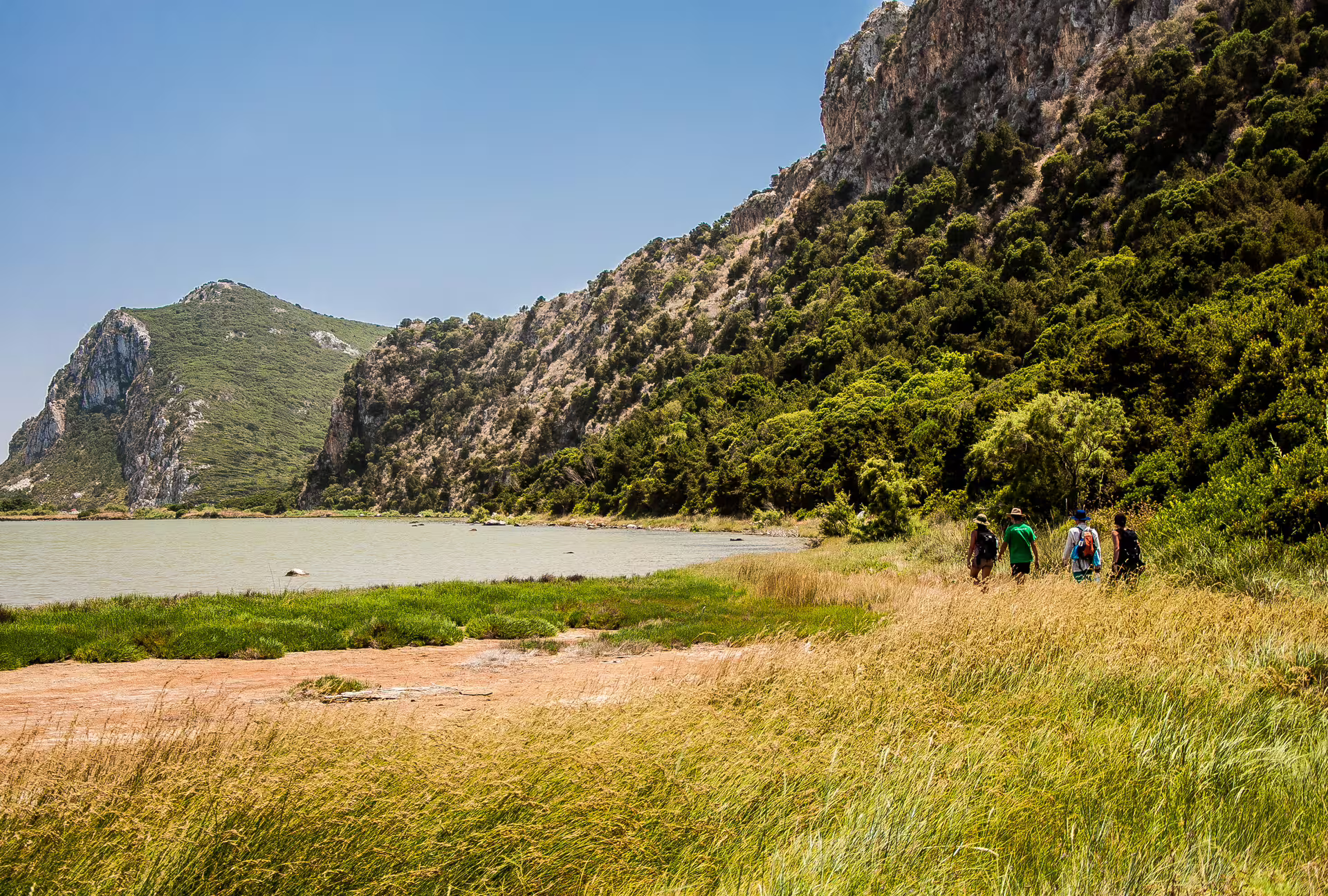 Small group hiking beside lagoon and limestone cliffs on Navarino Bay nature trail in Messinia, Greece