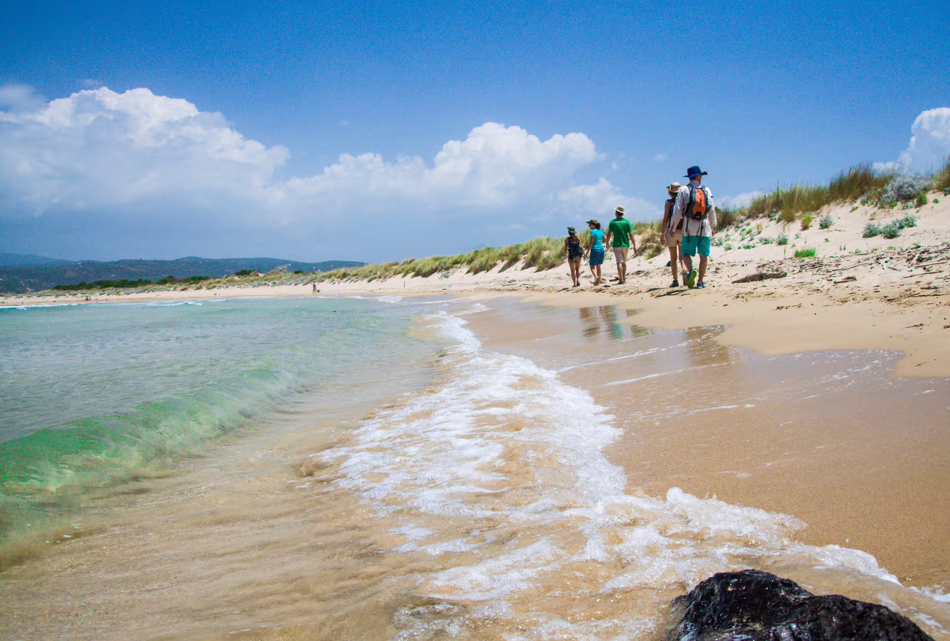 Small group hiking along sandy dunes and turquoise shoreline near Navarino Bay, Pylos, on a coastal trek