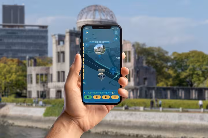 Hand holding smartphone with self-guided tour app in front of Hiroshima Atomic Bomb Dome