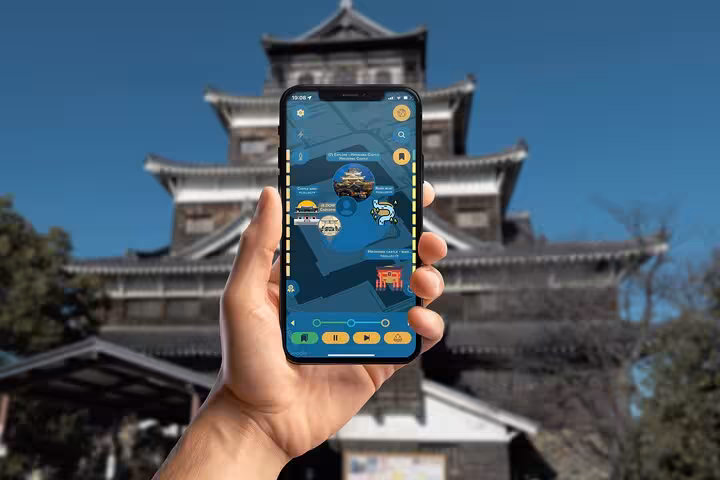 Hand holding smartphone with self-guided tour app in front of Hiroshima Castle, Japan