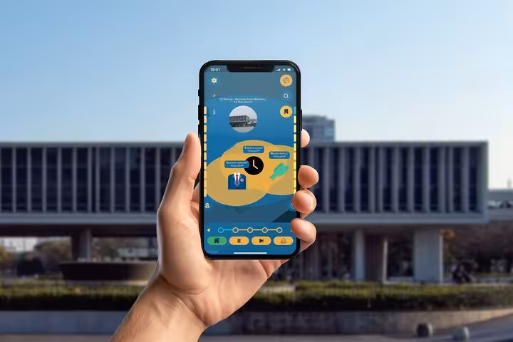 Hand holding smartphone displaying Hiroshima self-guided walking tour app with blue and yellow interface