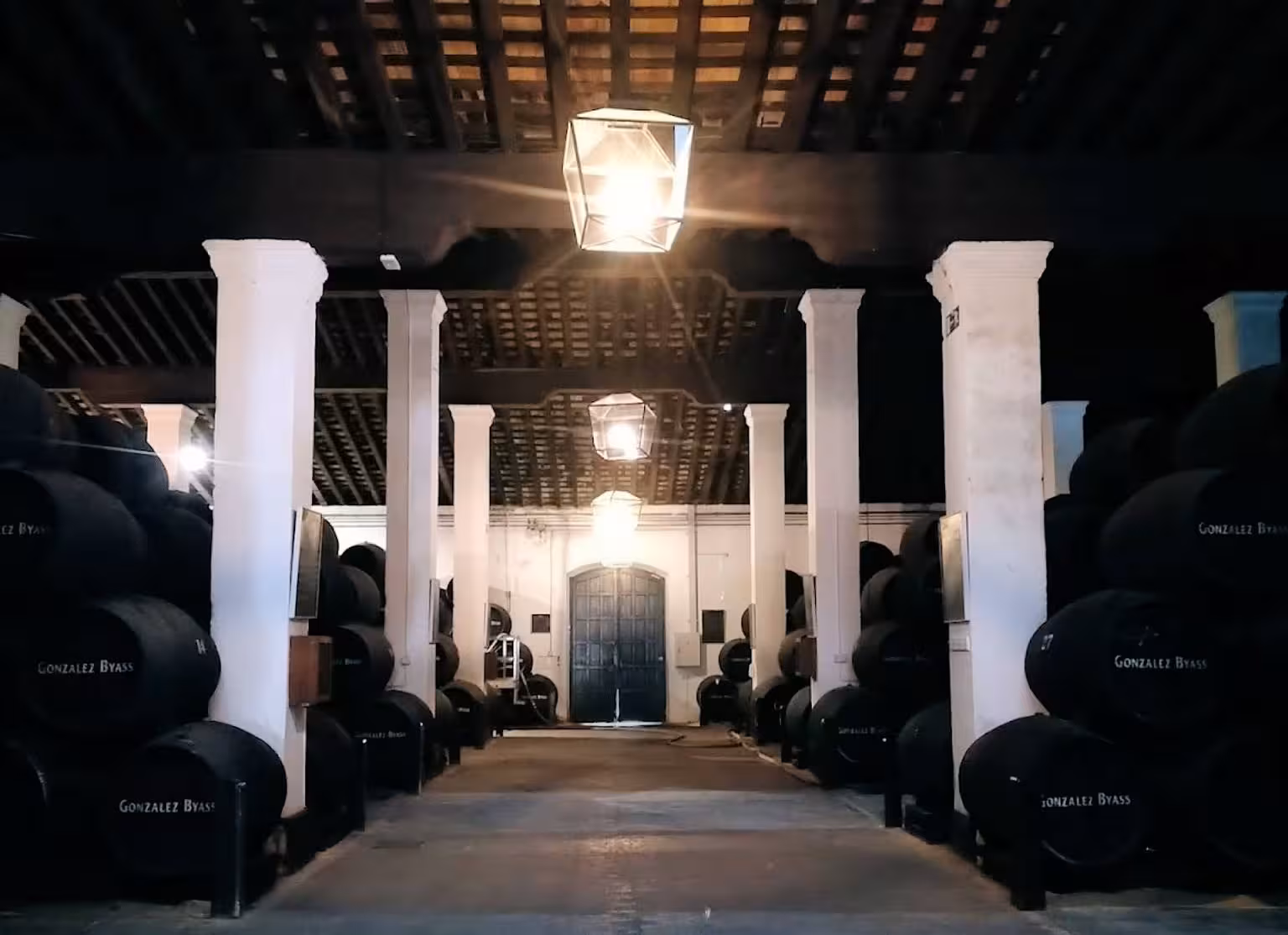 Historic bodega with rows of aging barrels, illuminated by warm lighting, ideal for a wine tasting experience.