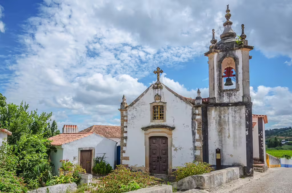 Historic Portuguese church with bell tower and rustic charm, set against a vibrant blue sky, perfect for religious tours.