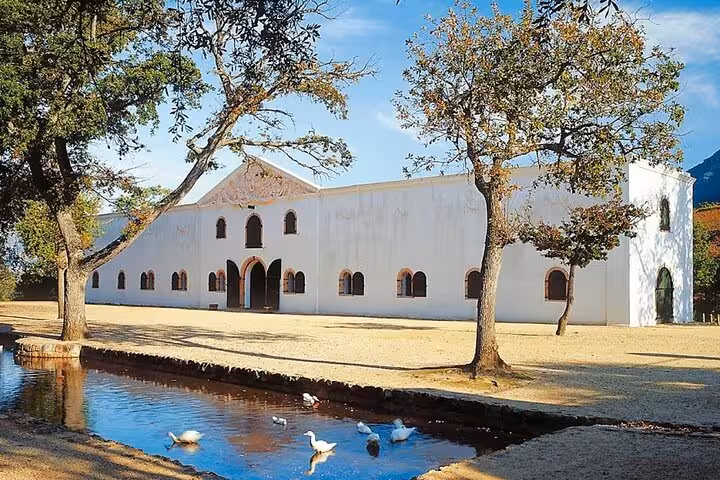 Historic white building with arched windows surrounded by trees and a pond, ideal for wine tasting tours.