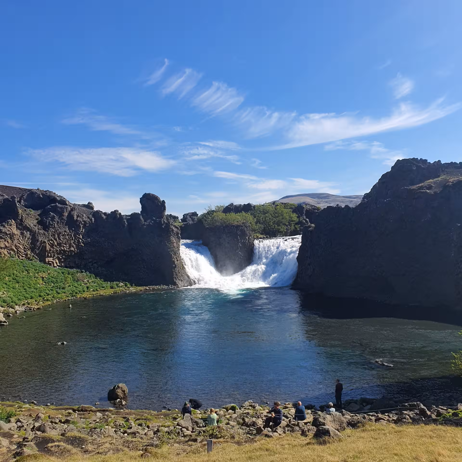 Hjálparfoss waterfall cascading into a turquoise pool surrounded by dark lava rocks in Iceland