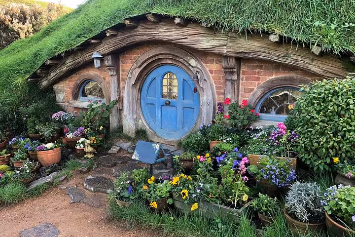 Charming Hobbiton house with a blue door and vibrant garden flowers, ideal for a scenic movie set tour.