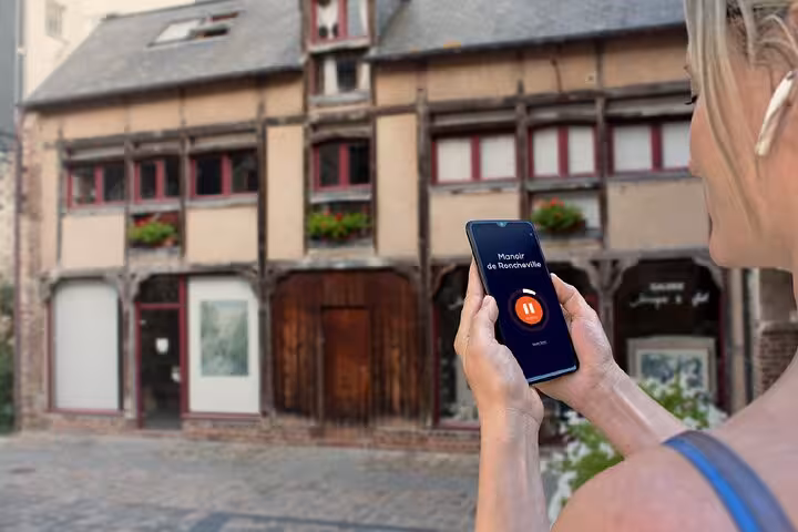 Tourist using audio tour app on smartphone in front of historic half-timbered building in Honfleur
