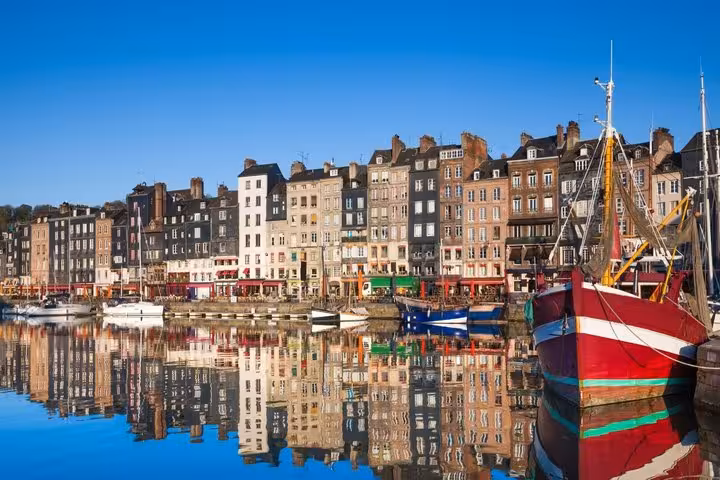 Colorful historic buildings reflecting in Honfleur harbor with moored fishing boats on a clear day