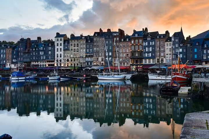 Honfleur harbor at sunset with sailboats and colorful Norman buildings reflected in calm water