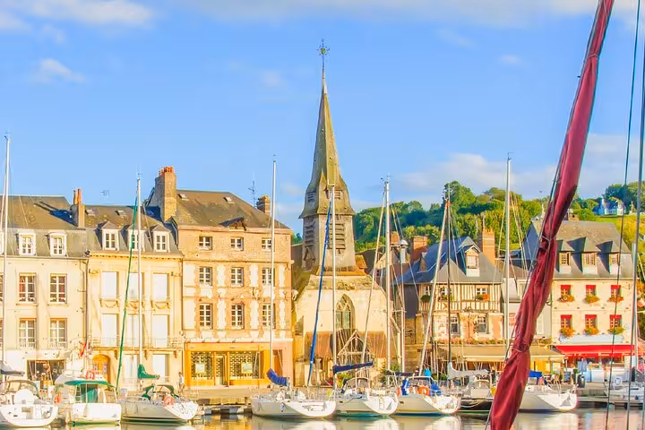 Honfleur harbour with sailboats, historic Norman buildings, and church steeple on a sunny day
