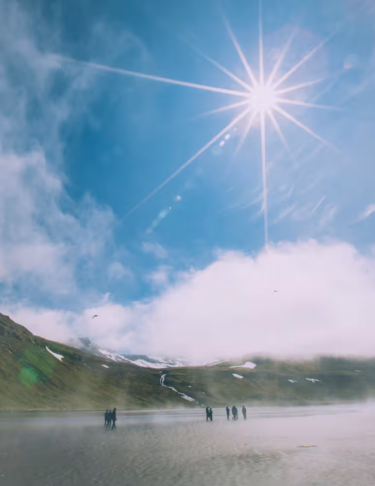 Hikers crossing a misty fjord under bright sun on the Hornstrandir Traverse hiking tour, Iceland