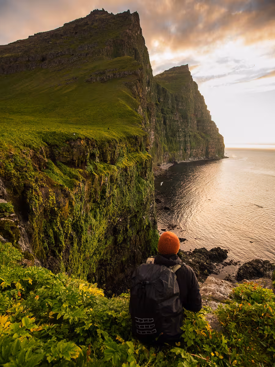 Traveler overlooking golden-hour Hornvík sea cliffs on Hornstrandir day tour, remote Westfjords Iceland coastline