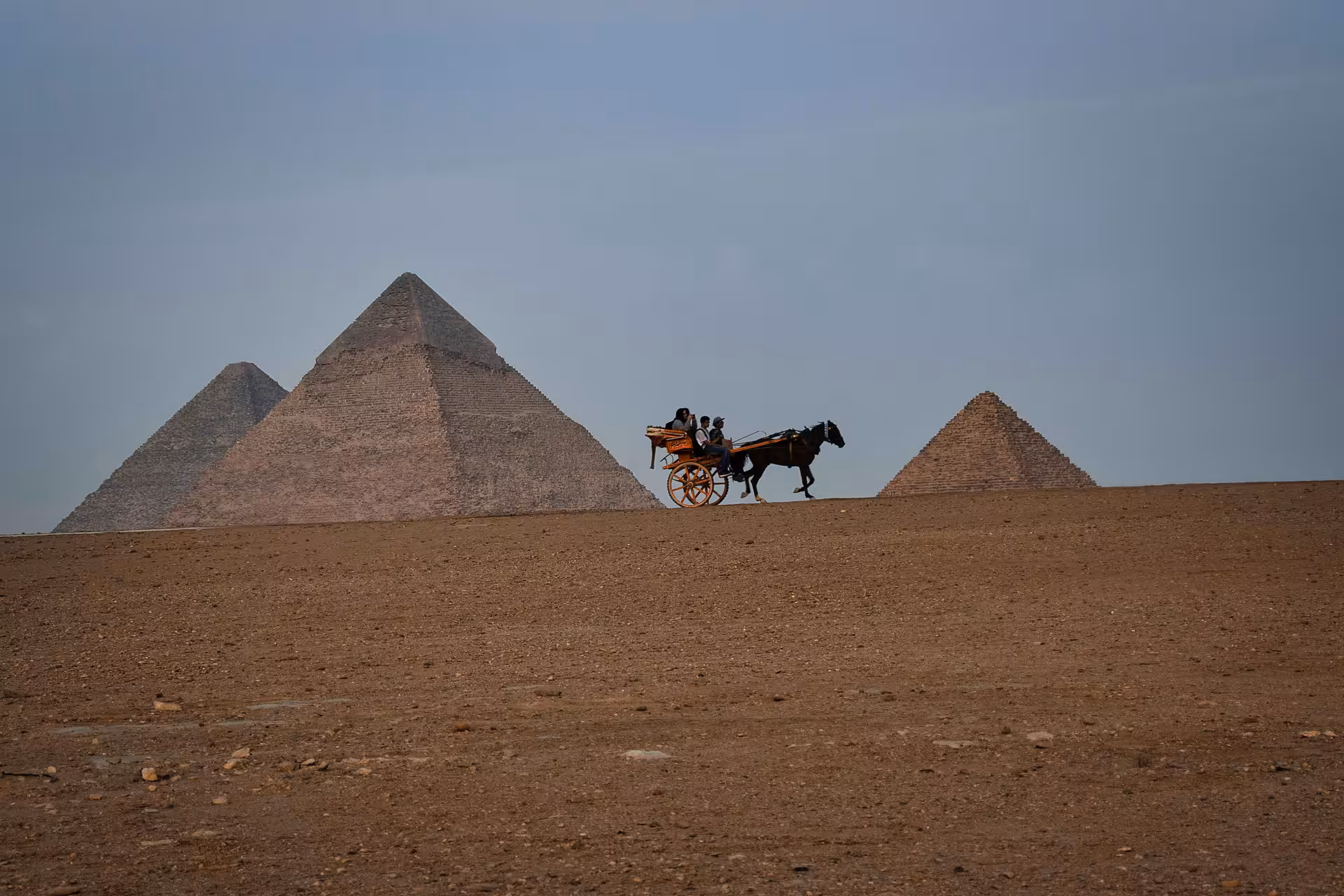 Horse-drawn carriage riding past the Great Pyramids of Giza on a sandy desert plateau