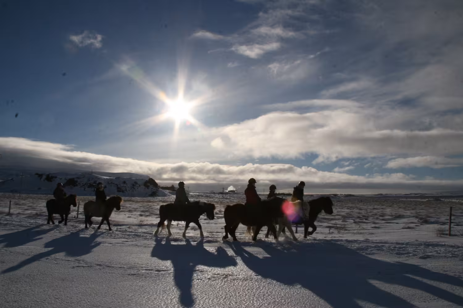 Silhouetted group horse riding across snowy plains at sunset on 05B Below the Mountains Iceland tour