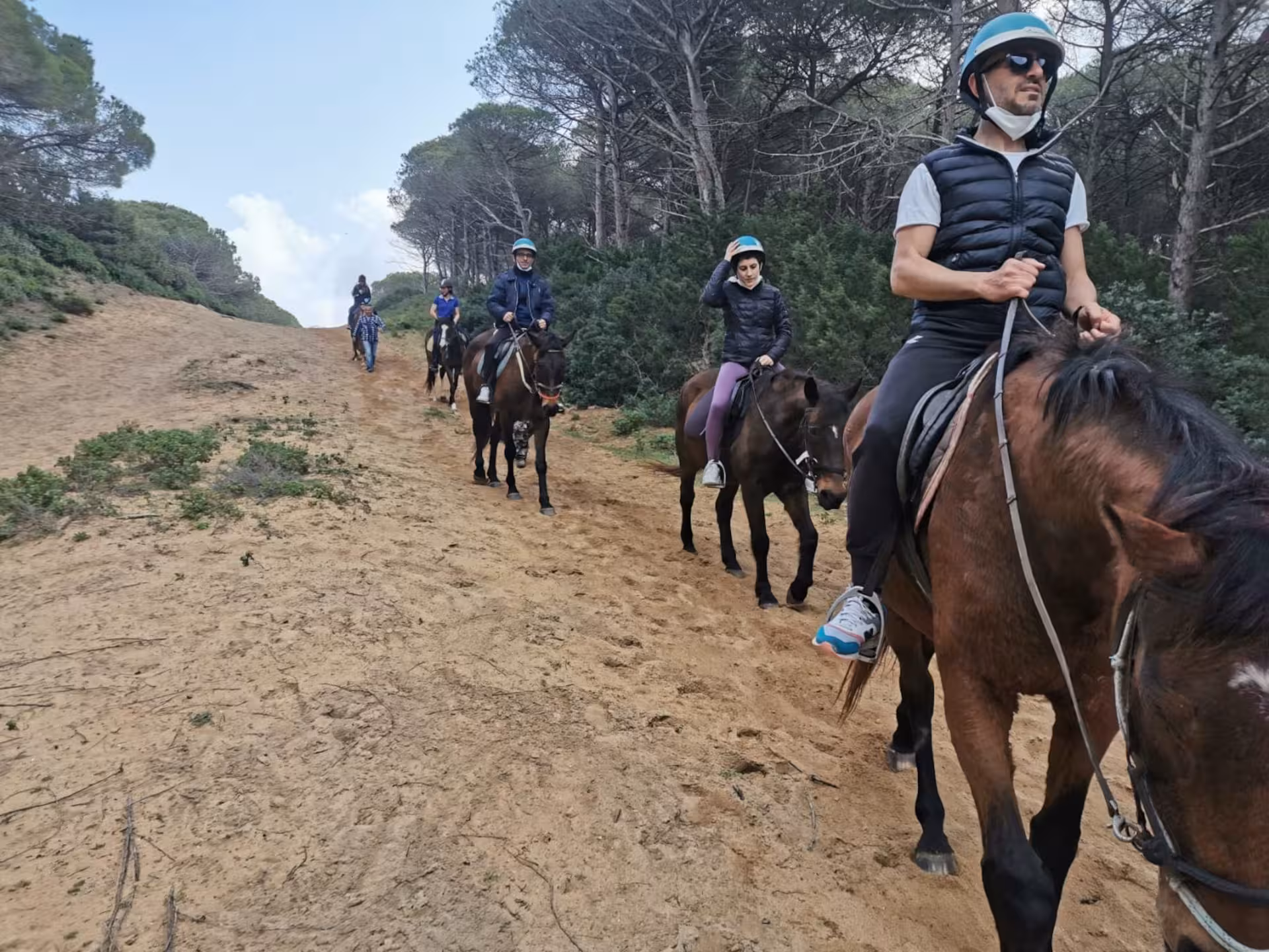 Riders enjoy a scenic horseback adventure through sandy trails in Lake Baratz, Alghero, surrounded by lush greenery.