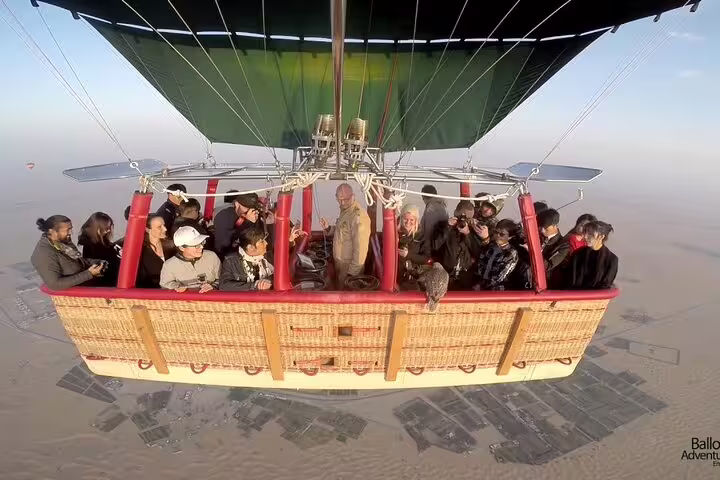 A group of tourists enjoy a breathtaking morning hot air balloon ride over the Dubai desert, capturing stunning aerial views.