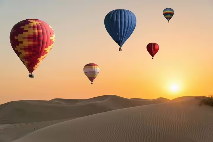 Colorful hot air balloons floating over Dubai's desert dunes at sunrise, offering a scenic morning adventure tour.