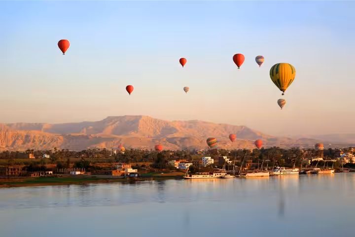 Hot air balloons drifting above the Nile River in Luxor at sunrise, with hotel pickup and drop-off service