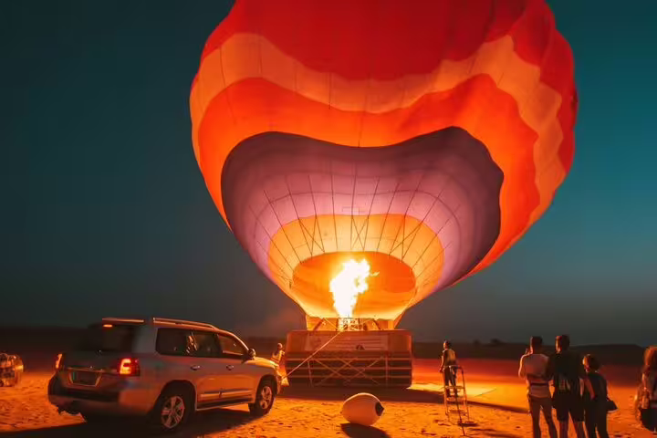 Hot air balloon inflating at sunrise in Dubai desert, ready for a magical morning tour with tourists and 4x4 vehicle nearby.