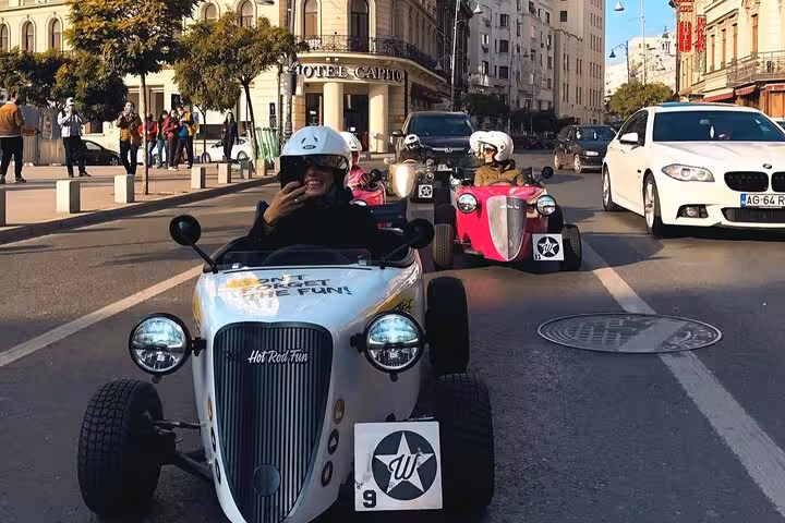 Tourists driving white and pink hot rod cars through Bucharest city streets near Hotel Capitol