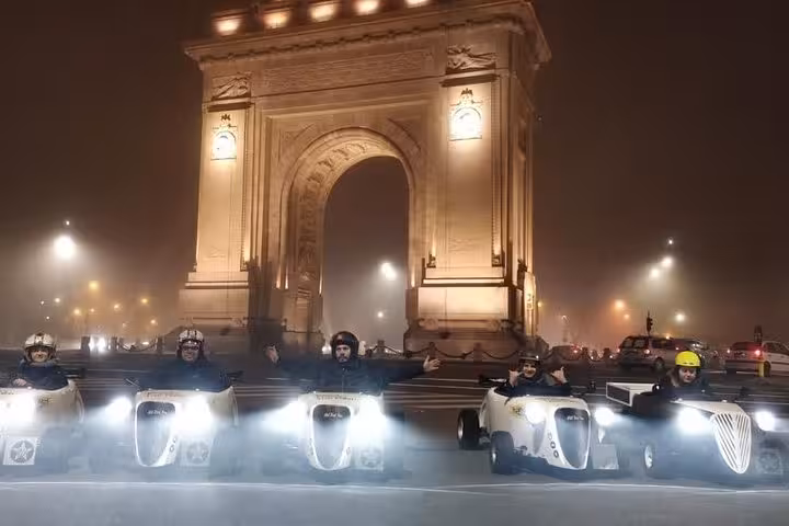 Hot rod cars lined up at night in front of the Arcul de Triumf in Bucharest