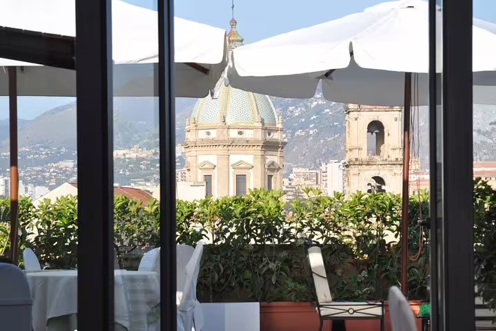 Rooftop terrace at Hotel Ambasciatori Palermo with umbrella-shaded tables and cathedral dome views before private airport transfer