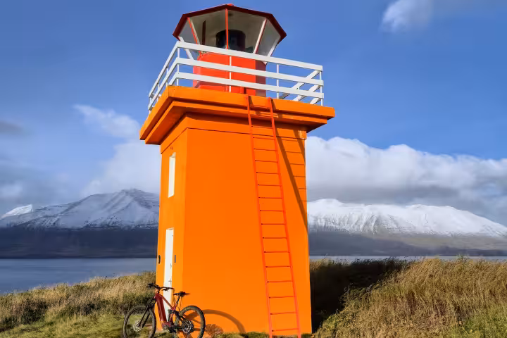 Bright orange lighthouse with ladder and red bicycle on Hrisey Island with snowy mountains in background
